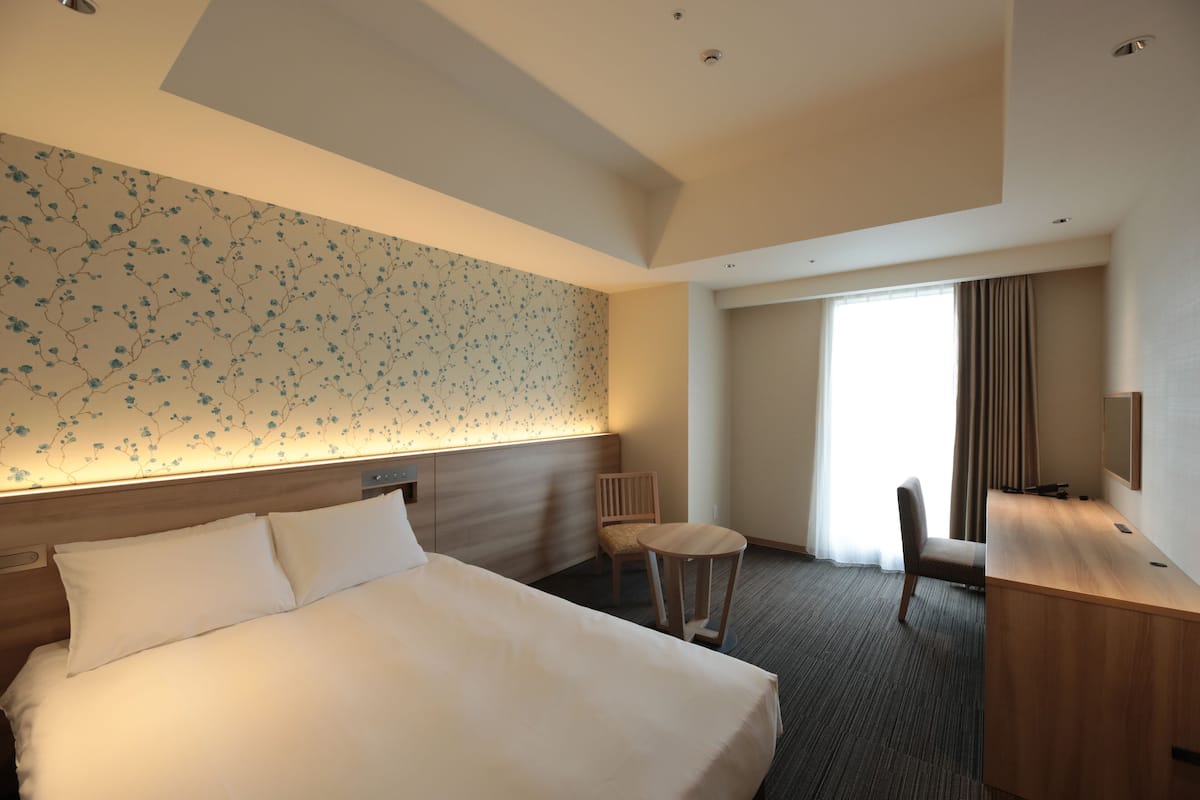 A hotel room with a large bed, a desk, a chair, and a window with curtains.
