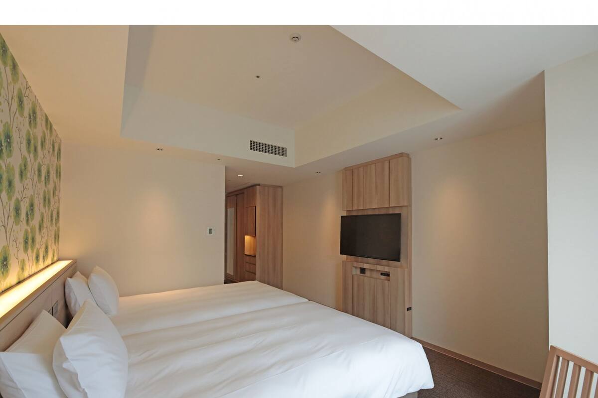 A hotel room with a large bed, a flat-screen TV, wooden cabinets, and a door leading to another room.