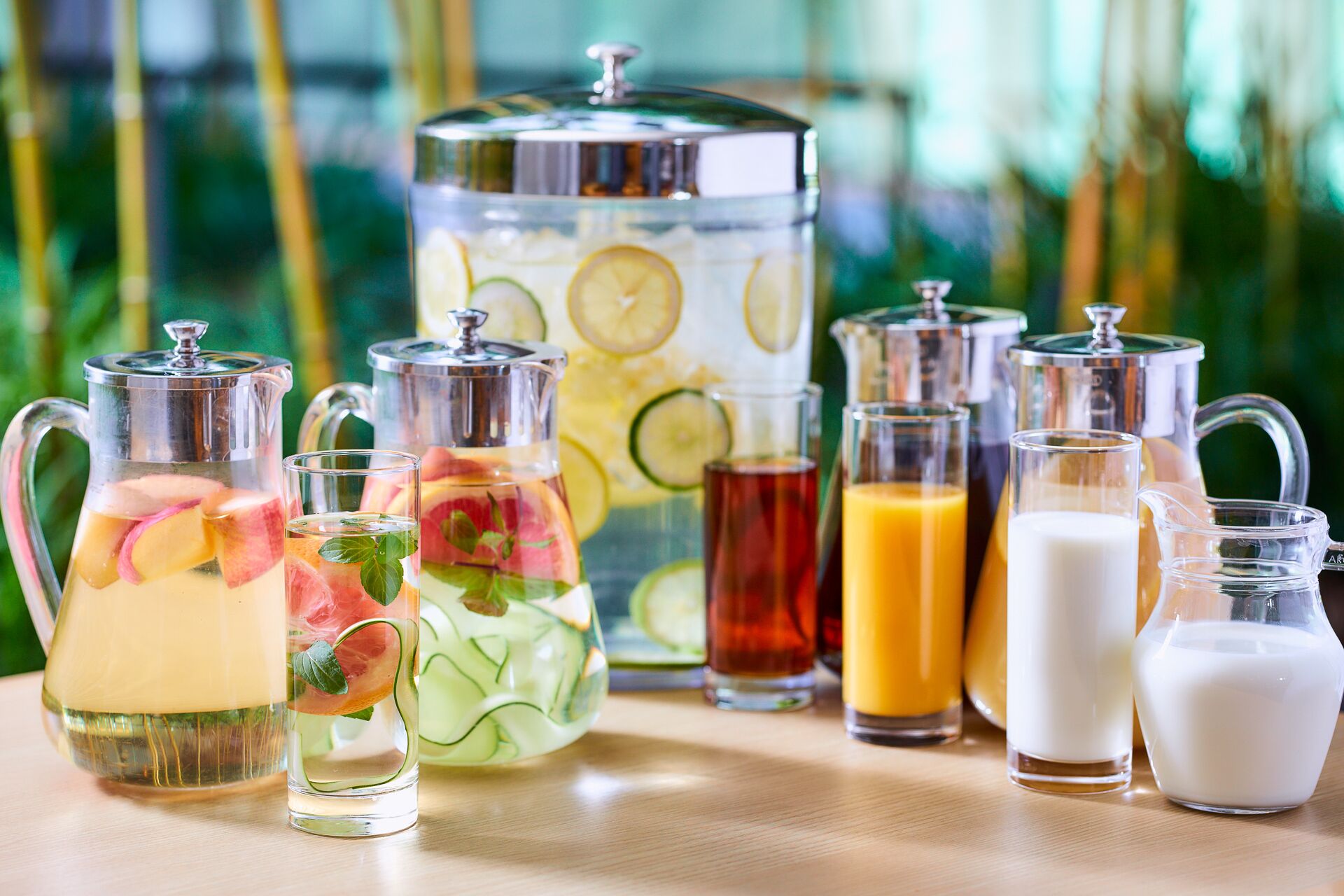 Variedad de bebidas en recipientes de vidrio y jarras, como agua, jugo y leche, dispuestas sobre una mesa.