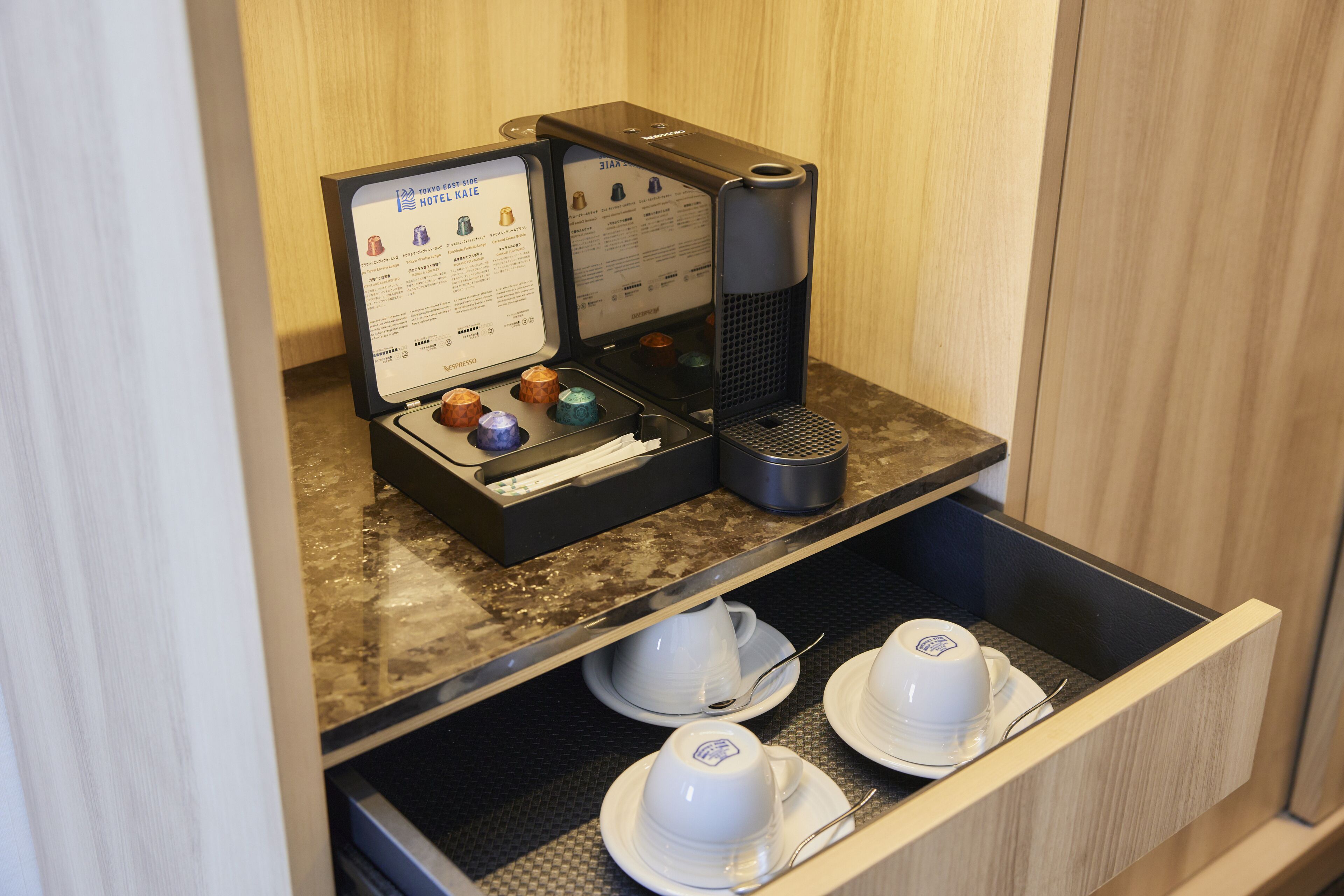 A coffee station with a menu, a coffee maker, and tea cups in a drawer.