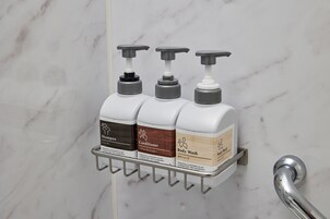 Kylpyhuone, jonka seinä on marmoria ja jossa on metallinen hylly, jossa on kolme pulloa erilaisia hygieniatuotteita.