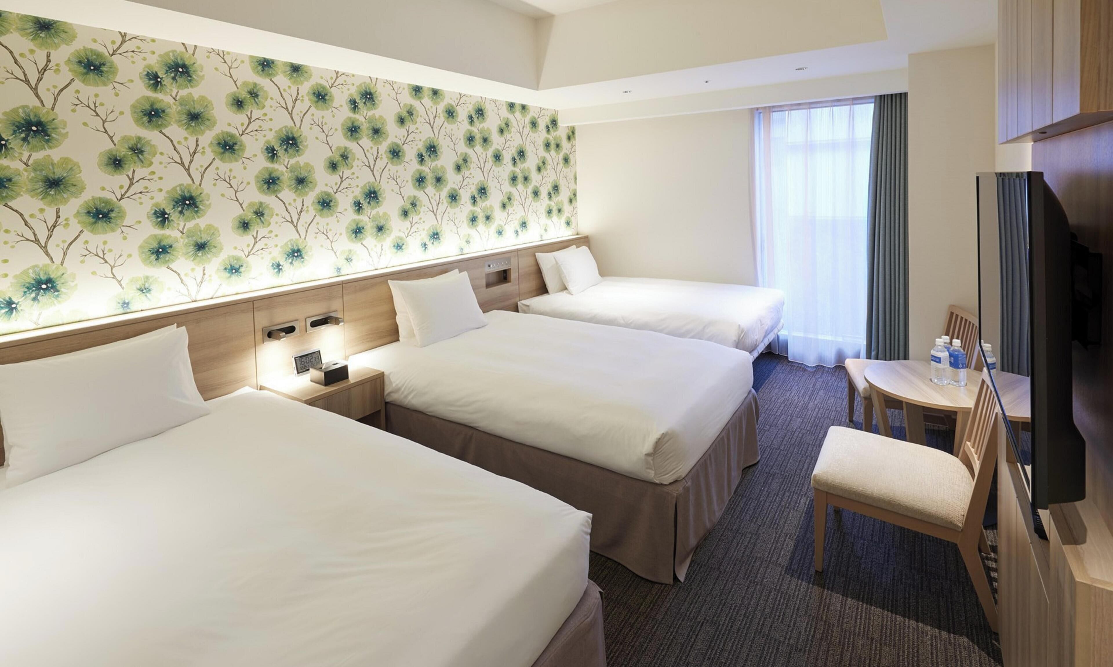Habitación de hotel con tres camas, un escritorio, una silla y un televisor.