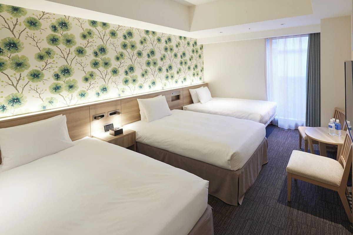 Habitación de hotel con tres camas, un escritorio, una silla y un televisor.