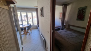A room with a bed, a dining table with chairs, a radiator, and a view of a balcony with a railing.