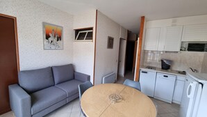 A compact living space with a grey sofa, a round wooden dining table, and a kitchenette with white cabinets and a microwave. - GRANDALLA  31 -1 apt 3 pers-Pas de la Casa- pie piste-006160 (PAS DE LA CASA)