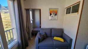 A living room with a grey sofa, a yellow pillow, a framed picture on the wall, and a view of a mountainous landscape through a window. - GRANDALLA  31 -1 apt 3 pers-Pas de la Casa- pie piste-006160 (PAS DE LA CASA)