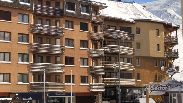 Un hotel a più piani con balconi, un cartello stradale e una montagna innevata sullo sfondo.