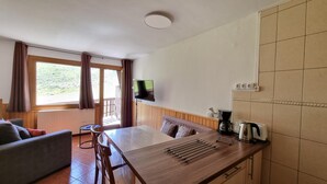 Una camera moderna con un tavolo da pranzo in legno, un divano, una TV a parete e un angolo cottura con macchina del caffè e bollitore.