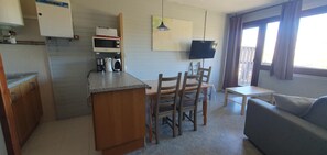 A compact kitchen with a microwave, coffee maker, and a small dining table with chairs. There is a sofa and a TV in the living area.