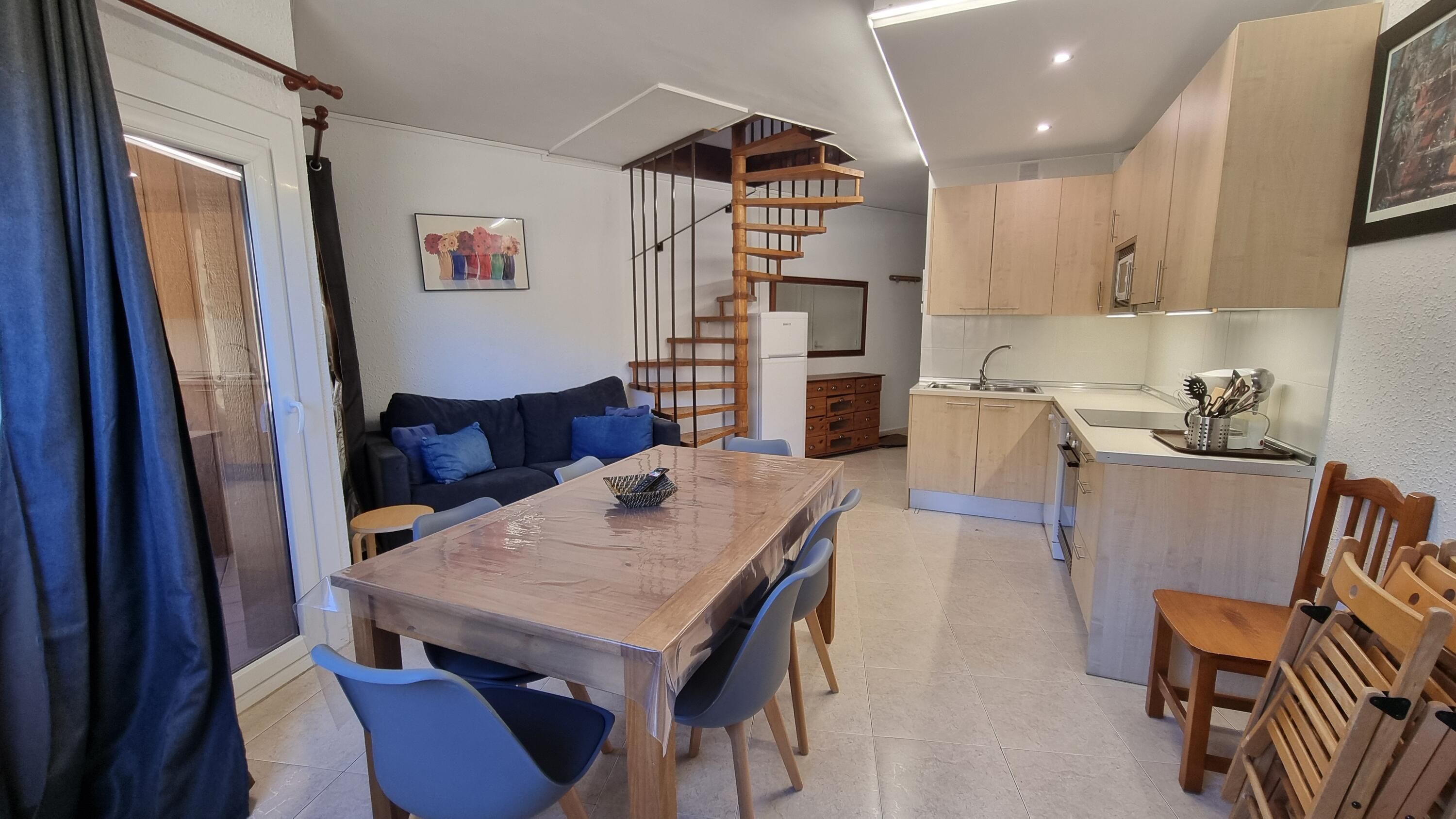 Een ruimtelijk ingerichte leefruimte met een eethoek, keuken en een trap naar een hoger gelegen niveau.