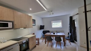 A compact kitchen with a microwave, oven, and sink. There is a dining table with chairs and a TV mounted on the wall.