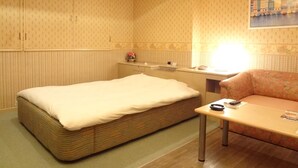 Una habitación con una cama individual, una mesita, un sofá y un cuadro en la pared.