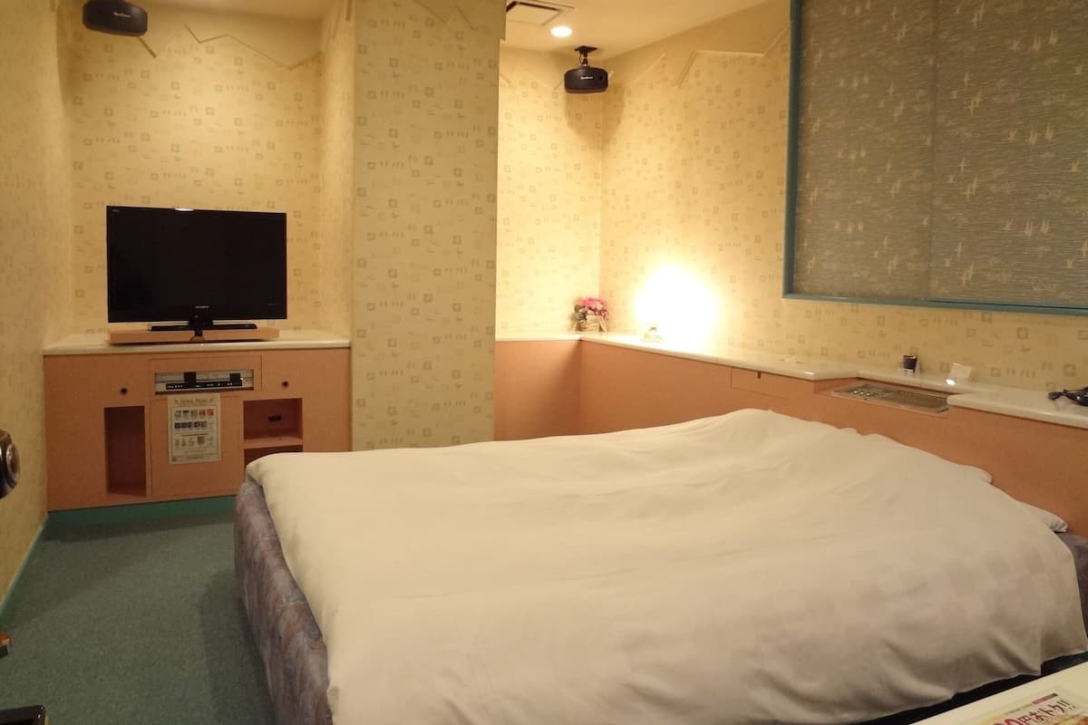 Une chambre d’hôtel avec un lit, un téléviseur posé sur un meuble, une petite armoire et une fenêtre donnant sur le ciel.