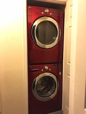 Een rode wasmachine en droger, gemonteerd aan de muur, in een smalle gang.
