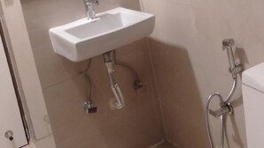 Un baño con lavamanos, espejo e inodoro. Se observan las tuberías y un calentador de agua sobre el lavamanos.