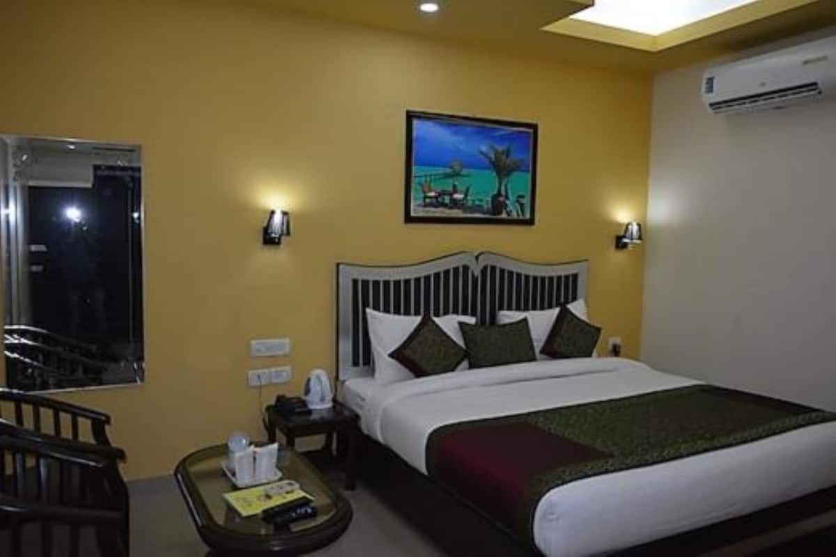 A hotel room with a bed, a nightstand, a chair, a small table, and a painting on the wall.