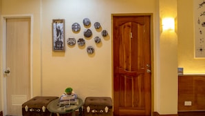 A room with a wooden door, a wall-mounted light, a small round table with a plant, and a wall with circular photographs. - U Feel Home (Cebu City)