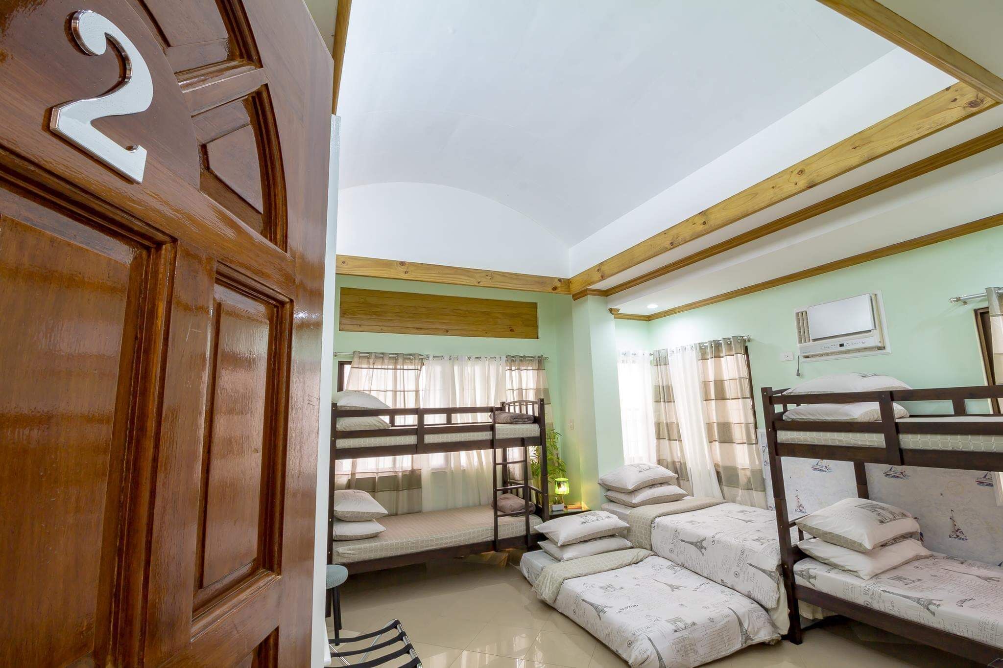 Una habitación con literas, una puerta de madera con un número y una ventana con cortinas.