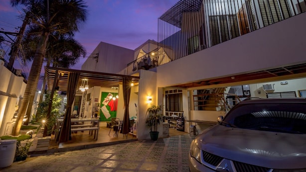 A modern building with a covered outdoor seating area, a car parked in front, and a balcony with a railing. - U Feel Home (Cebu City)