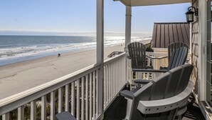 Ein Balkon mit Blick auf Strand und Meer. Auf dem Balkon befinden sich Stühle und ein Tisch.