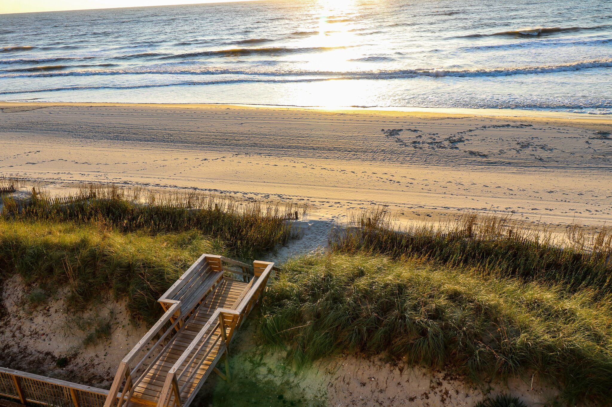 A beach with a wooden boardwalk leading to the water, surrounded by grass and sand.