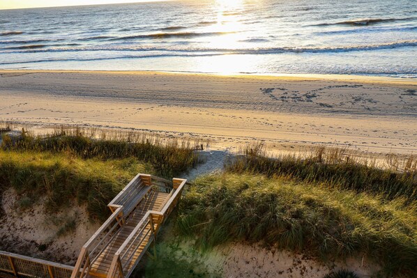 A beach with a wooden boardwalk leading to the water, surrounded by grass and sand.