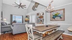 A dining area with a wooden table and benches, a gray sofa, a chandelier, and a television.