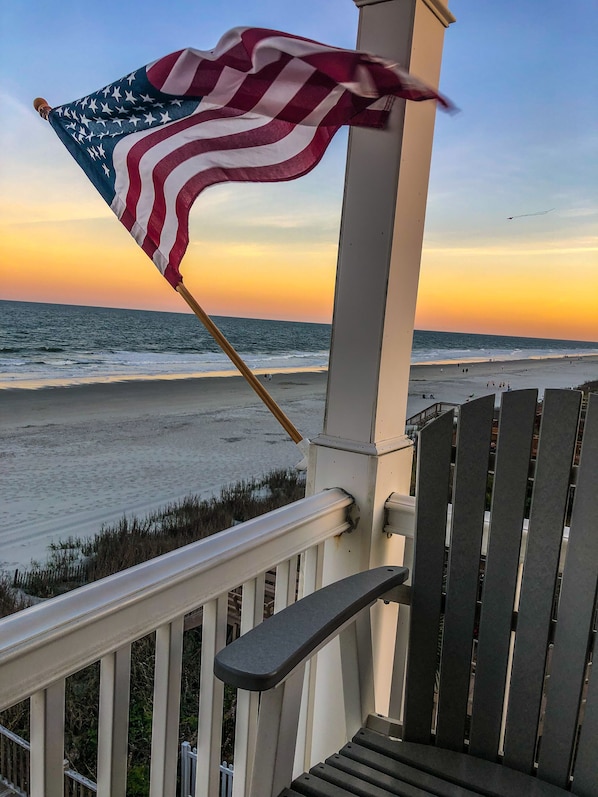 A balcony with a view of the beach and ocean during sunset.