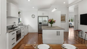 A modern kitchen with white cabinetry, stainless steel appliances, and a wooden dining table set for two. - The Keeper's House (East Toowoomba)