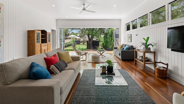 A modern living room with a large sofa, coffee table, and a view of the backyard through large windows. - The Keeper's House (East Toowoomba)