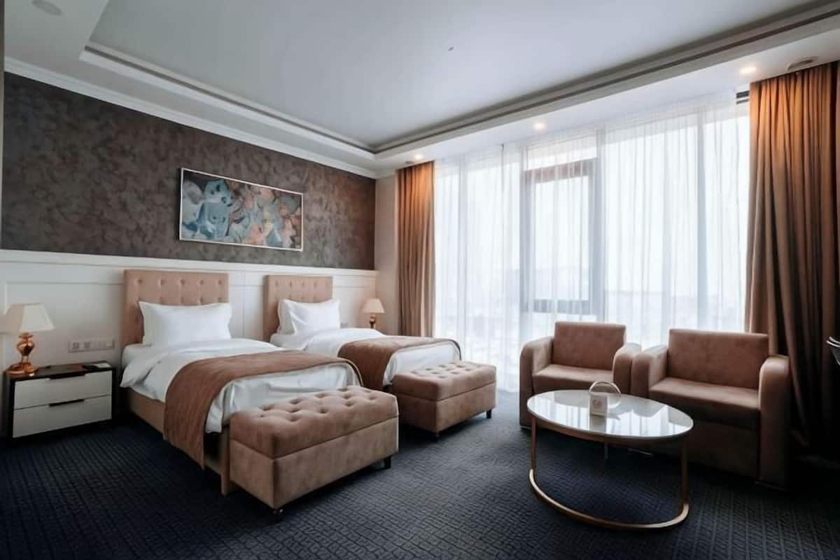 A hotel room with two beds, a sofa, a coffee table, and a large window with curtains.
