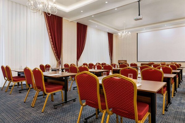 A conference room with red chairs, tables, a projector screen, and a chandelier. - Ramada by Wyndham Shymkent (Shymkent)