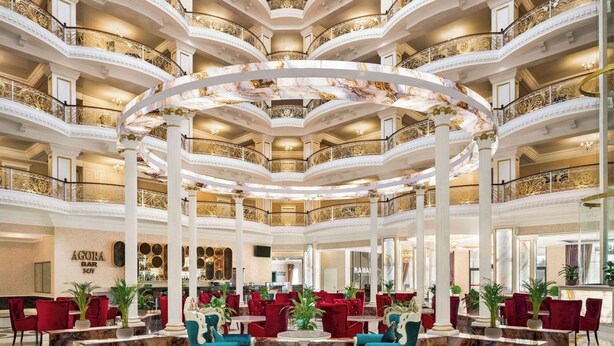 A grand lobby with marble flooring, red and blue seating, and a central circular decorative element. - Ramada by Wyndham Shymkent (Shymkent)