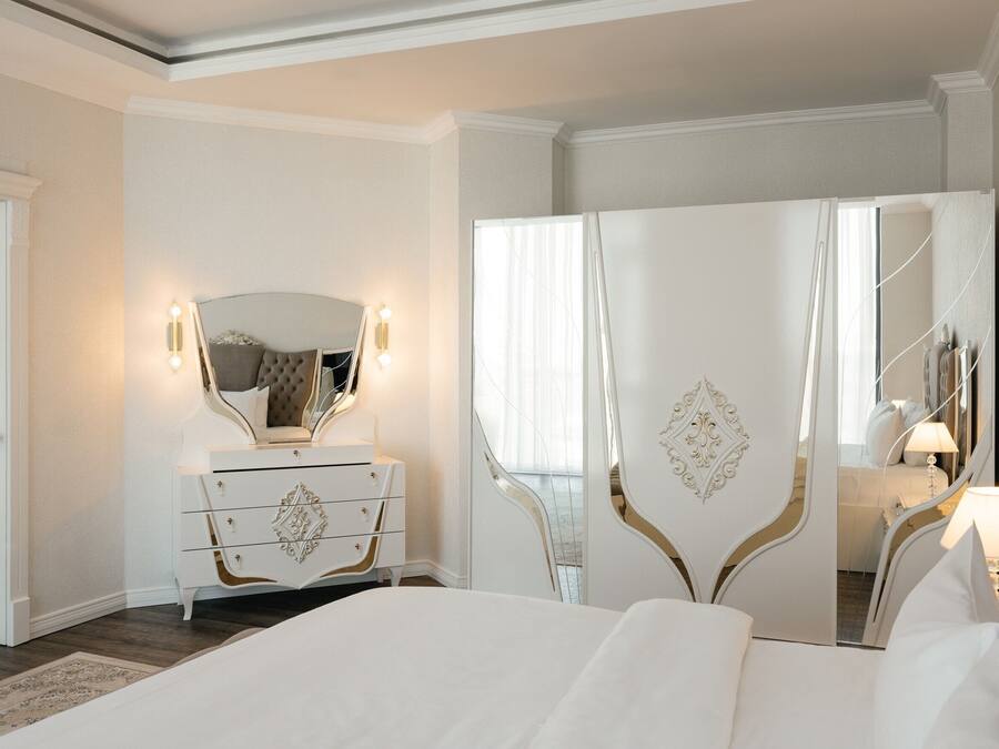 A bedroom with a large bed, a dresser with drawers, a mirror, and a wardrobe.