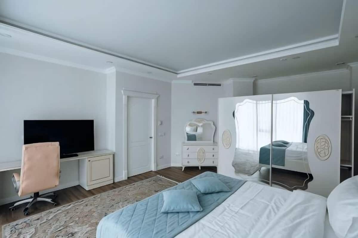 A bedroom with a bed, a TV, a wardrobe, and a desk.