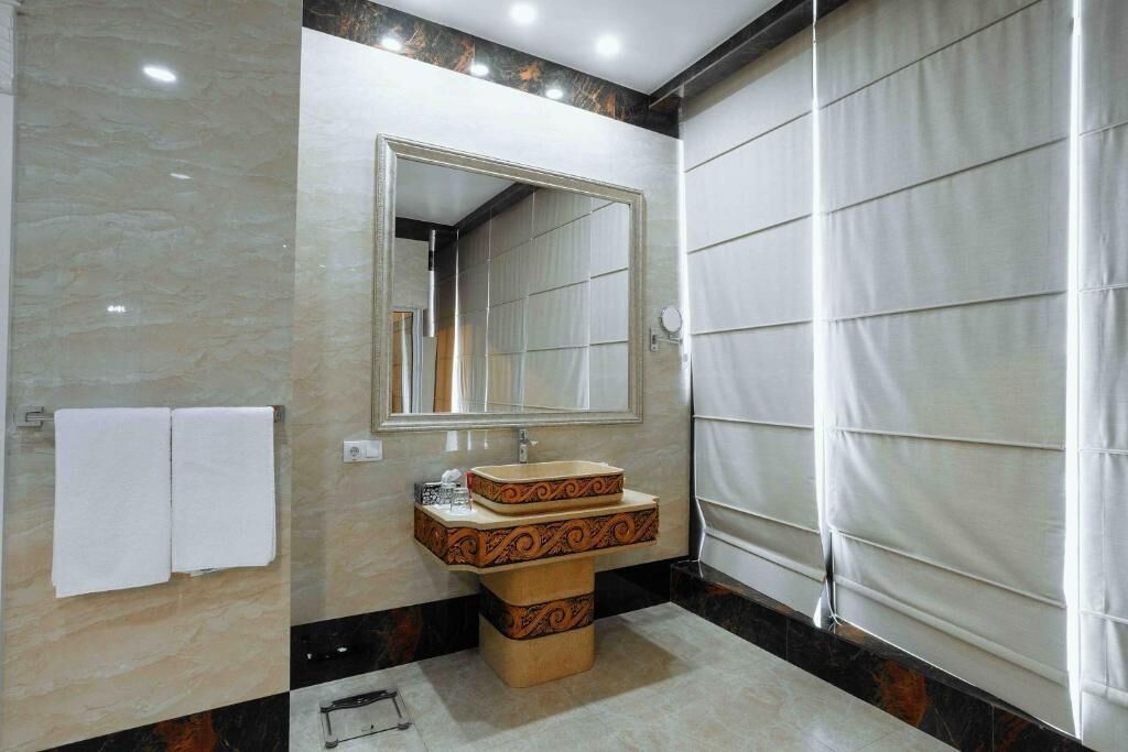 A bathroom with a marble floor, a sink with decorative tiles, a large mirror, and a towel rack.