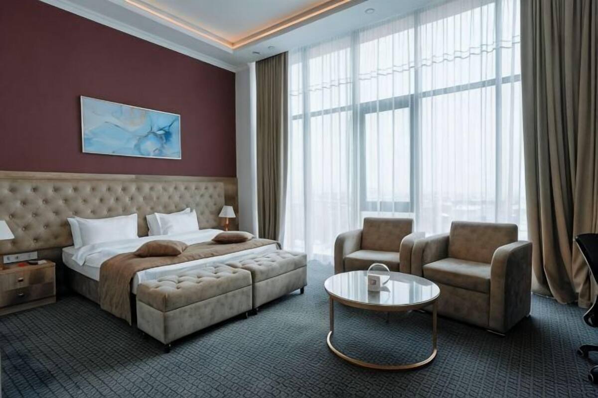 A hotel room with a large bed, a sofa, a round coffee table, and a view of the city.