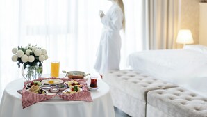 A hotel room with a breakfast table set with various dishes, a vase with flowers, and a person in a robe. - Ramada by Wyndham Shymkent (Shymkent)