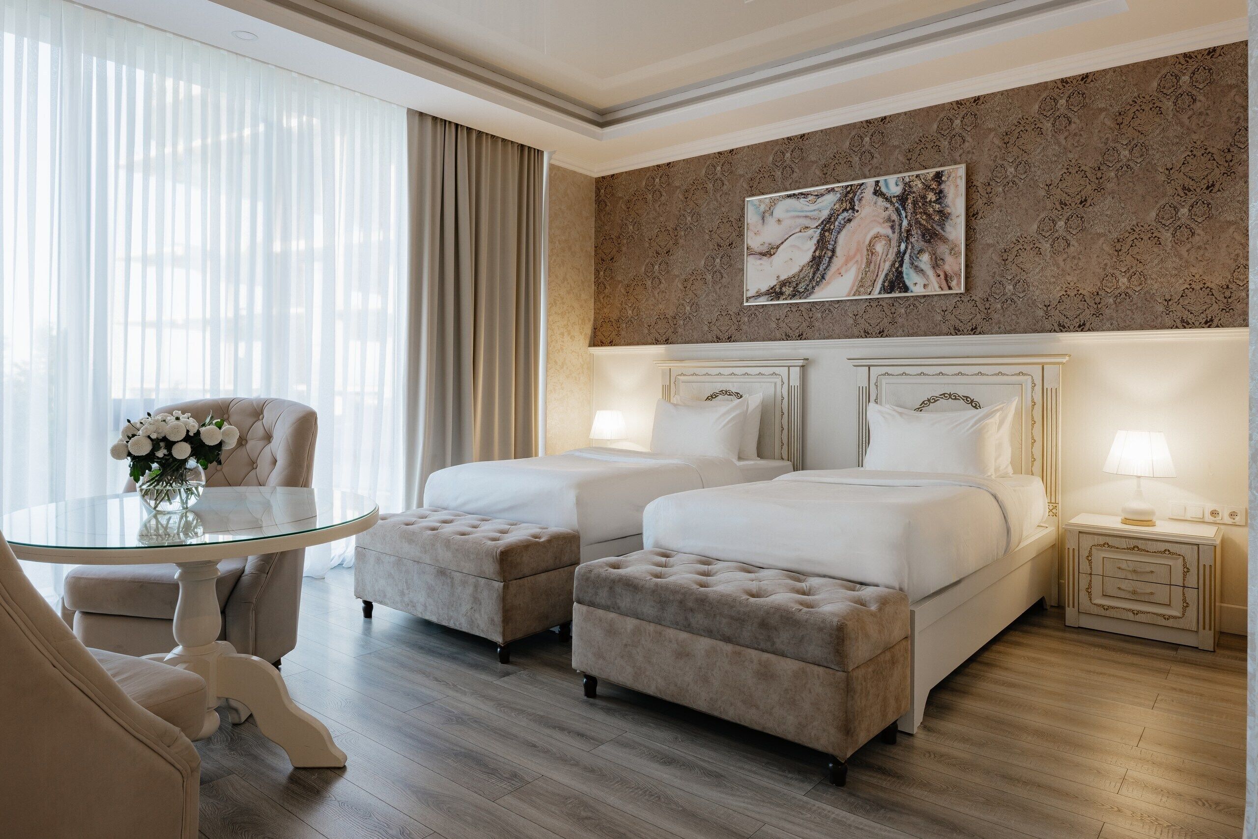 A hotel room with two beds, a glass table, a chair, and a decorative painting on the wall.