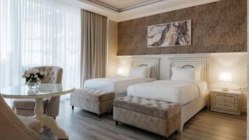 A hotel room with two beds, a glass table, a chair, and a decorative painting on the wall.