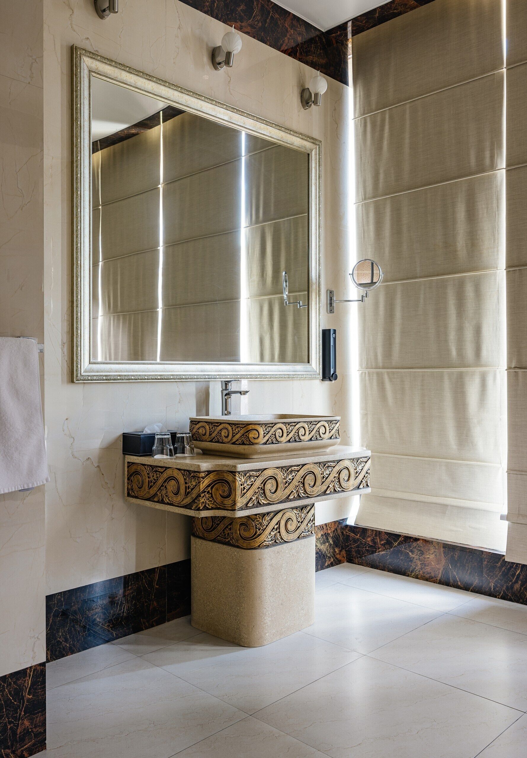 A bathroom with a large mirror, a sink with ornate designs, and a tiled floor.