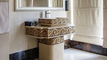 A bathroom with a large mirror, a sink with ornate designs, and a tiled floor.