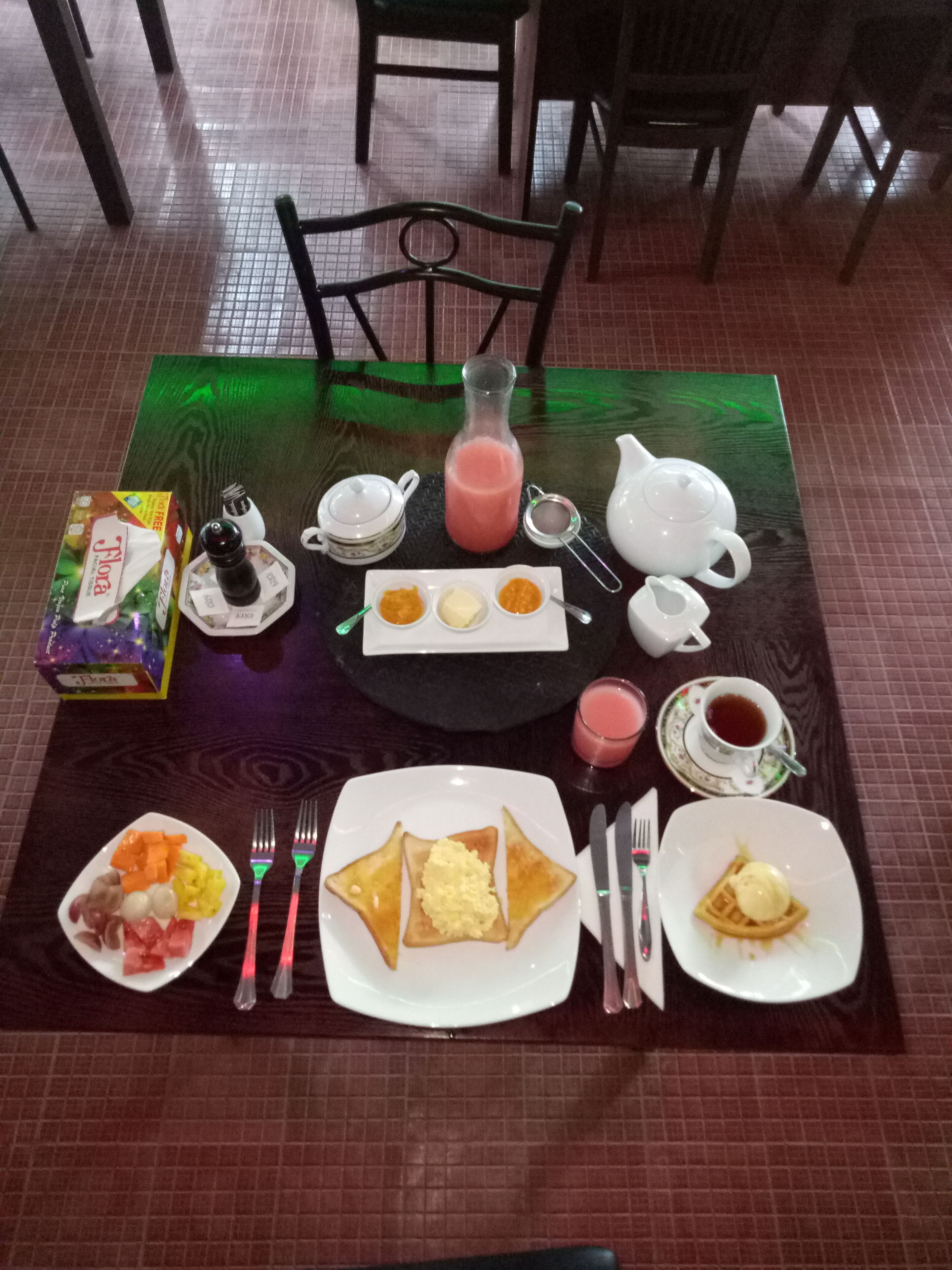 A breakfast setting with a table set for two, including plates of food, a pitcher of juice, and various breakfast items.