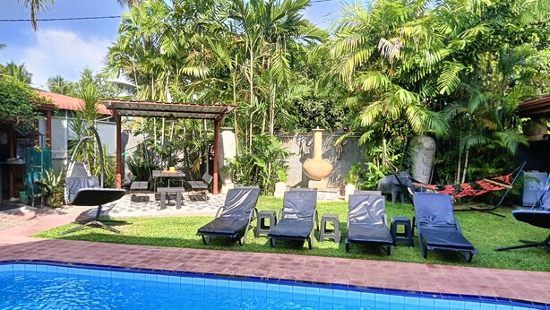 Uma área de piscina com espreguiçadeiras, mesa e pérgola.