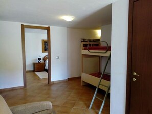 A room with a bunk bed, a wooden door, a small table with a lamp, and a framed picture on the wall.