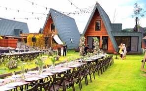 Une réception de mariage organisée en plein air, avec plusieurs tables où les invités sont assis, et une scène pour les discours.