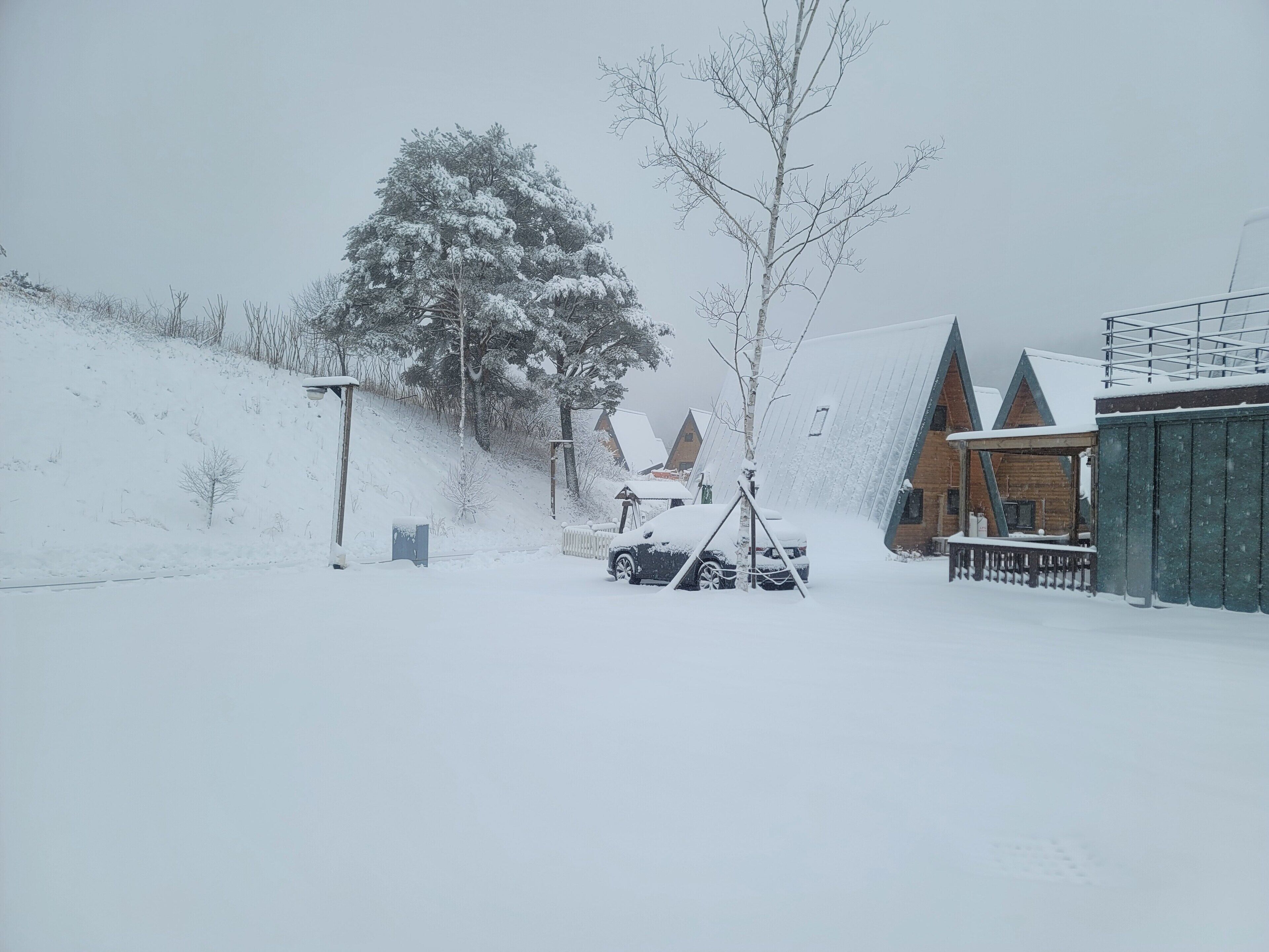A snowy landscape with a wooden cabin and a car parked in front.