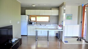 A modern kitchen with white cabinets, a microwave, and a sink. There's a dining table with metal legs and a television on a wooden stand.