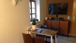 Un comedor con una mesa de madera, cuatro sillas, un televisor montado en la pared, un pequeño árbol de Navidad y un cráneo de vaca decorativo en la pared.