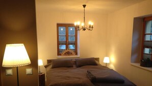 Un dormitorio con una cama grande, dos lámparas de noche, un candelabro, una ventana con vistas y una mesita de noche.